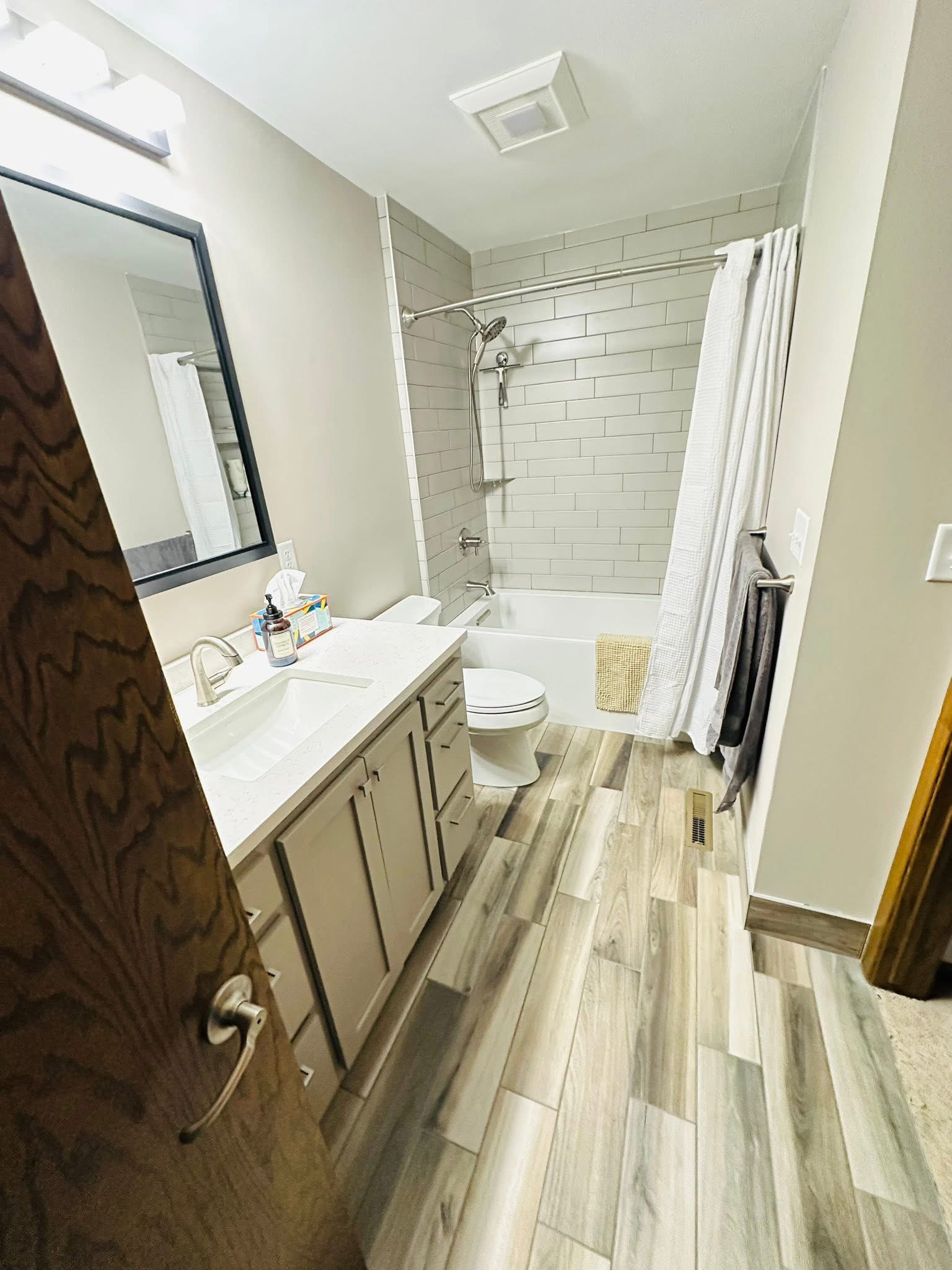 Bathroom with a light subway tile tub surround and wood-look plank floor.