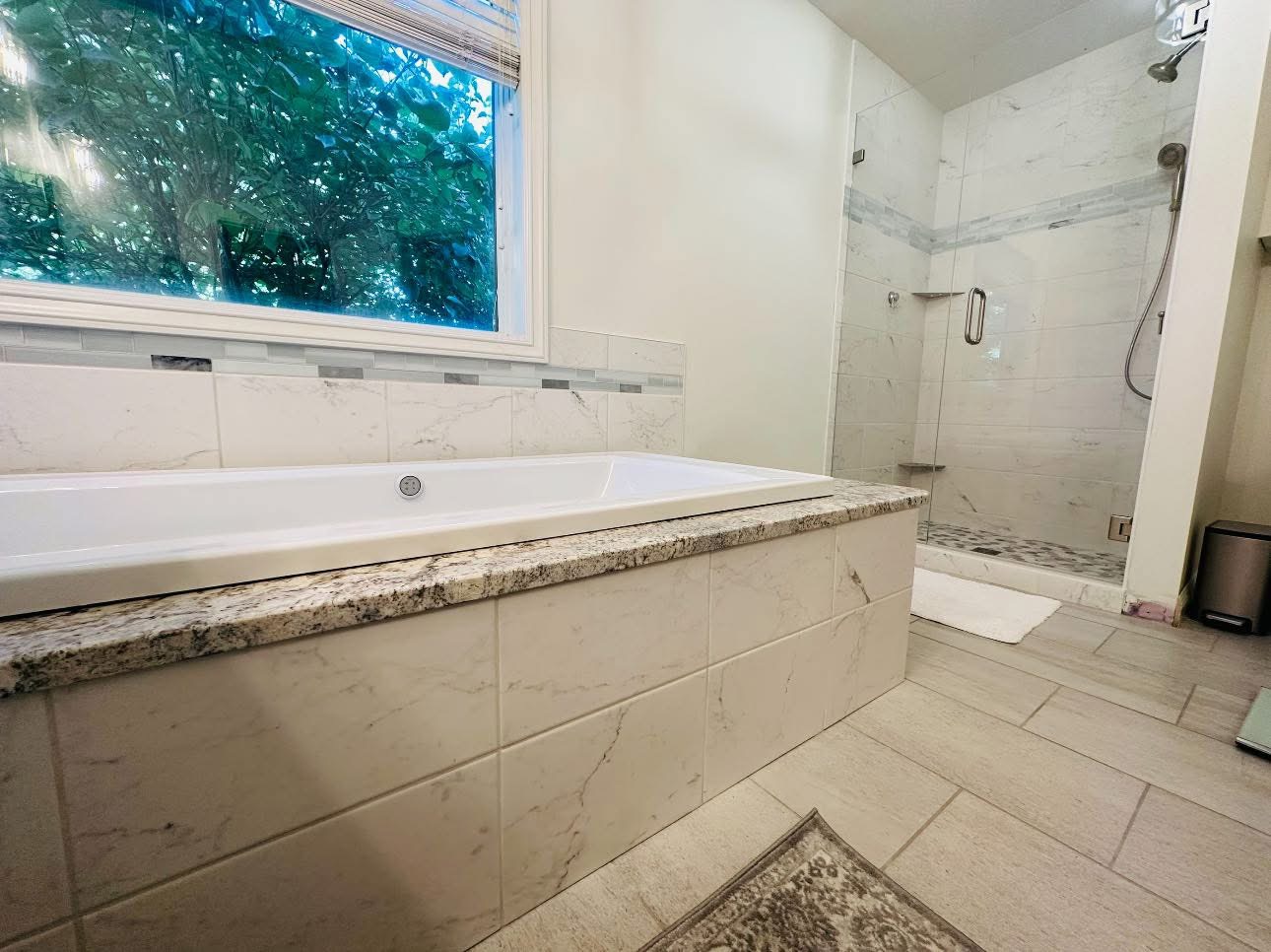 Light stone-look tile across a tub surround, bathroom floor, and separate glass shower.